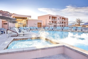 A swimming pool with lounge chairs, a poolside area, and a building with balconies. - Moab | Adventure Retreat | Pool + Hot Tub | 2BR (Moab)