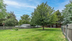 A residential backyard with a lawn, a wooden fence, and a house with a garage. - Lake It Easy - NNY Waterfront Home on Lake Ontario (Dexter)