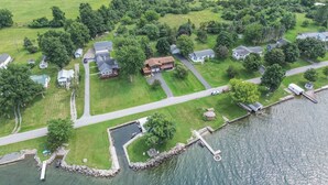 An aerial view of a residential area with houses, a dock, and a small water body. - Lake It Easy - NNY Waterfront Home on Lake Ontario (Dexter)