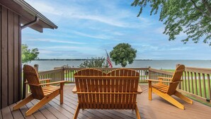 A wooden deck with two Adirondack chairs facing a lake, a flag, and a tree. - Lake It Easy - NNY Waterfront Home on Lake Ontario (Dexter)