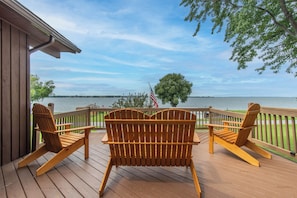Eine Holzterrasse mit zwei Adirondack-Stühlen, die auf einen See blicken, einer Flagge und einem Baum.