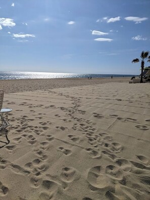 Ein Strand mit Fußabdrücken im Sand, ein Stuhl und eine Palme.