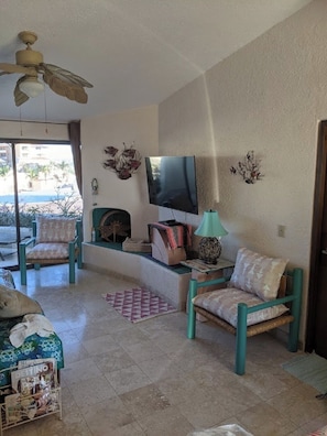 Ein Wohnzimmer mit Deckenventilator, Flachbildfernseher, Kamin und Blick ins Freie.