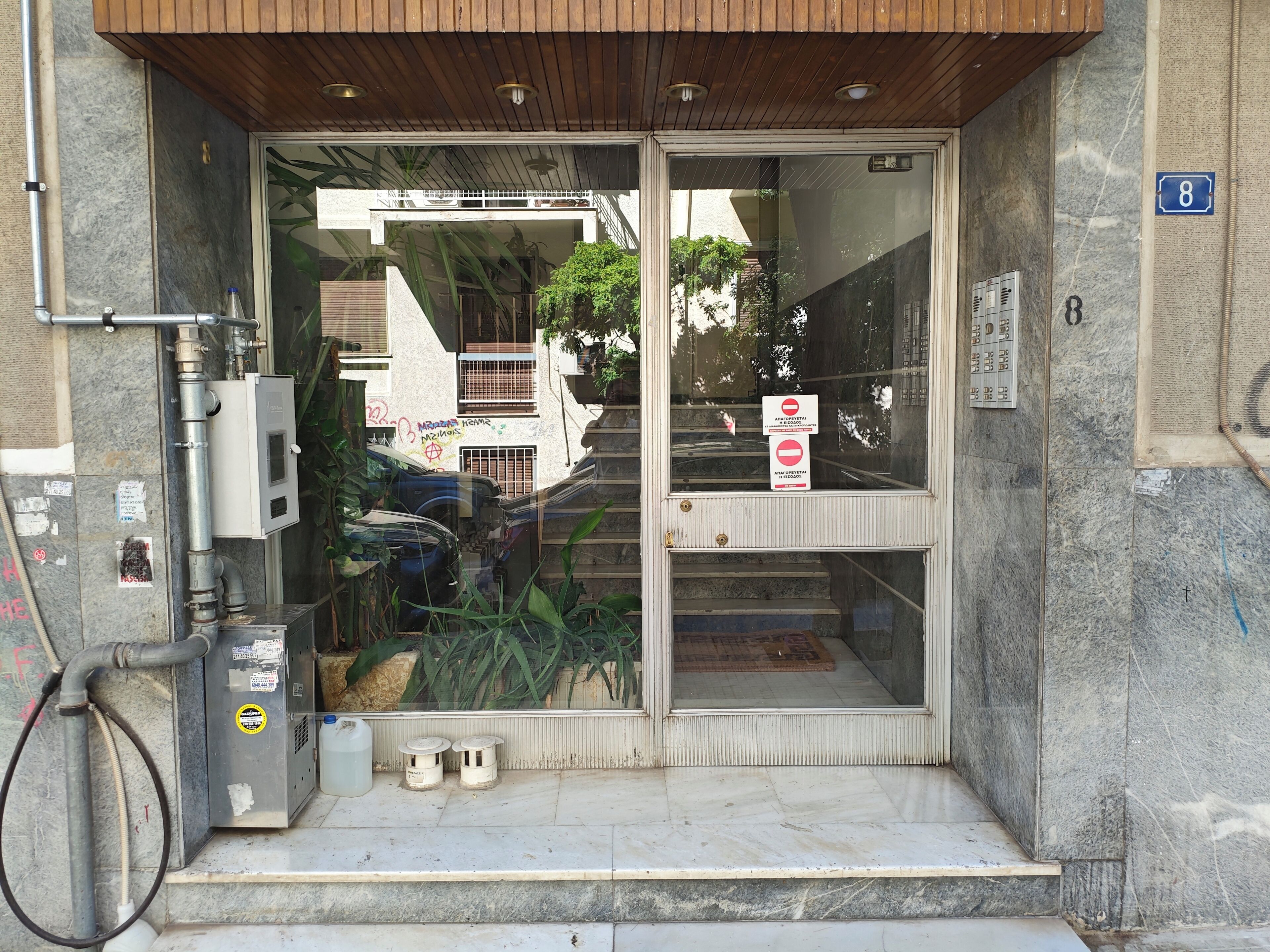 A building entrance with a glass door, a metal utility box, and a number sign.