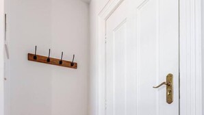 Un pasillo con piso de madera, paredes blancas y una puerta blanca con picaporte de latón.