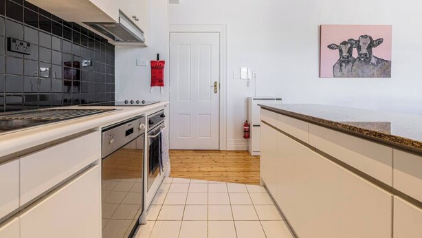 Cocina con estufa, horno y salpicadero de azulejos. Se observa una puerta blanca y un extintor de incendios colgado en la pared.