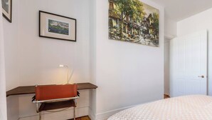 Un dormitorio con cama, escritorio y silla, un cuadro en la pared y una puerta.