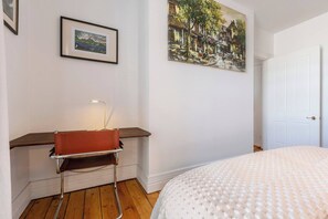Ein Schlafzimmer mit Bett, Schreibtisch mit Stuhl, einem Bild an der Wand und einer Tür.