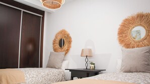 A hotel room with two beds, a nightstand, a lamp, and decorative wall mirrors.