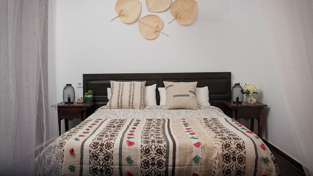 A bedroom with a dark wooden headboard, a patterned bedspread, and a hanging light fixture.