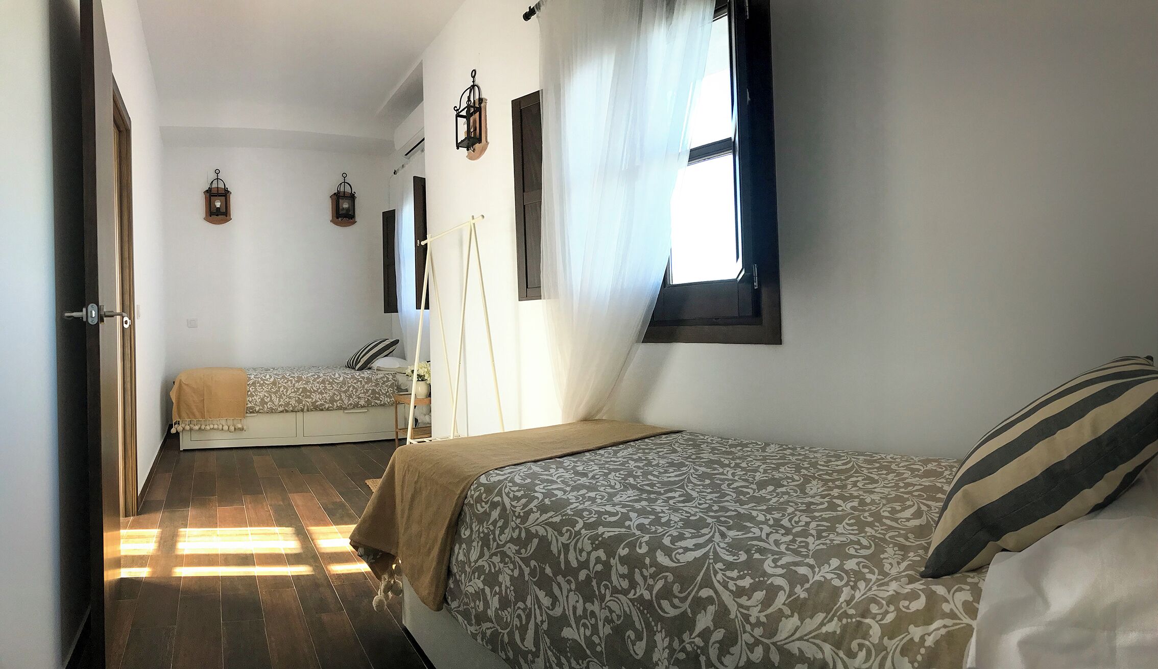 A room with two beds, a window with curtains, and a hanging light fixture.