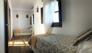 A room with two beds, a window with curtains, and a hanging light fixture.