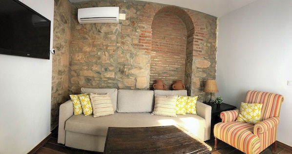 A living room with a stone wall, a sofa, a patterned armchair, and a television.