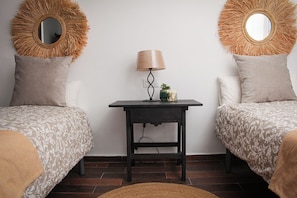 A room with two beds, a small table with a lamp, and two wall-mounted mirrors.
