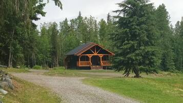 Une cabane dotée d’un porche, entourée d’une forêt.