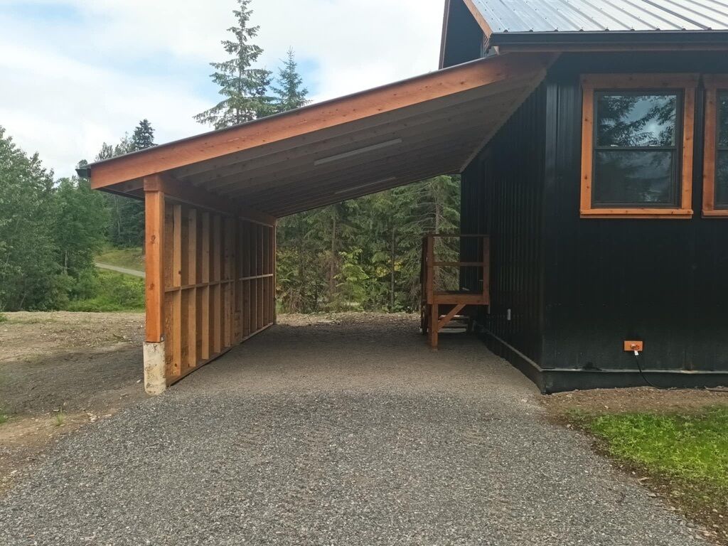 Un espace extérieur abrité, avec un chemin de gravier menant à un bâtiment doté d’un toit en métal.
