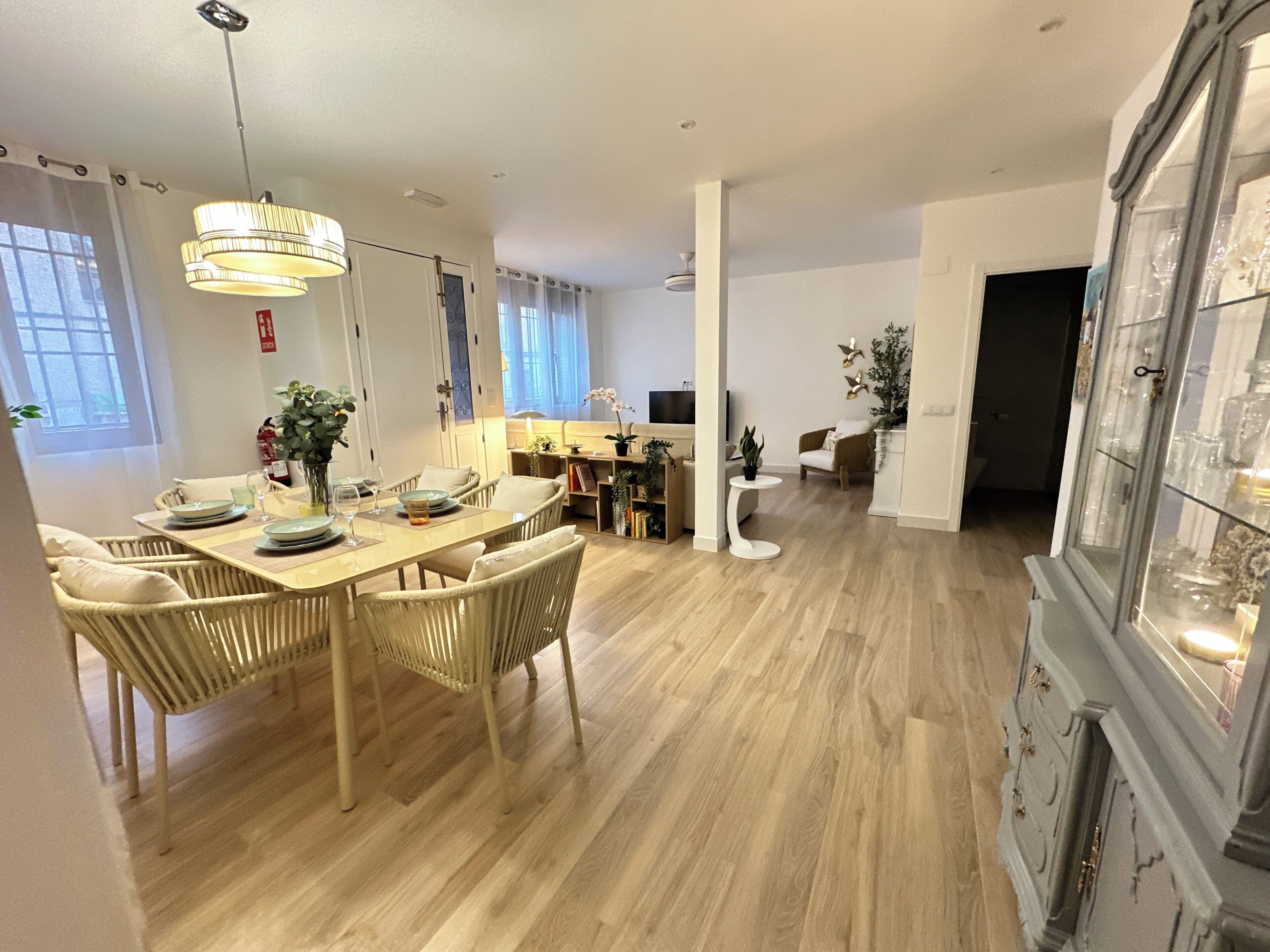 Un comedor con una mesa y sillas de madera, una araña y un aparador con puertas de cristal.