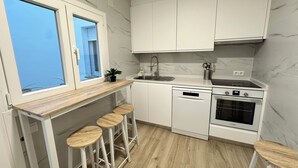 A compact kitchen with white cabinets, a wooden countertop, a sink, a dishwasher, and a stove. There are three stools under the countertop.