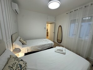 A hotel room with two beds, a bedside table, a lamp, a mirror, and a window with curtains. - La Posada Manchega Planta baja (Consuegra)
