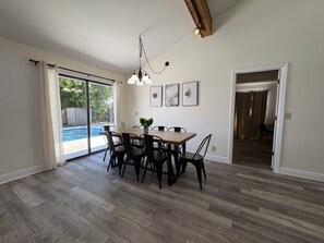 A dining area with a wooden table and chairs, a hanging light fixture, and a view of a swimming pool through glass doors. - Rocky Point Retreat - Private Pool - Boat Parking - 3BR (Stuart)