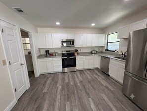 A modern kitchen with white cabinets, stainless steel appliances, and a grey wooden floor. - Rocky Point Retreat - Private Pool - Boat Parking - 3BR (Stuart)