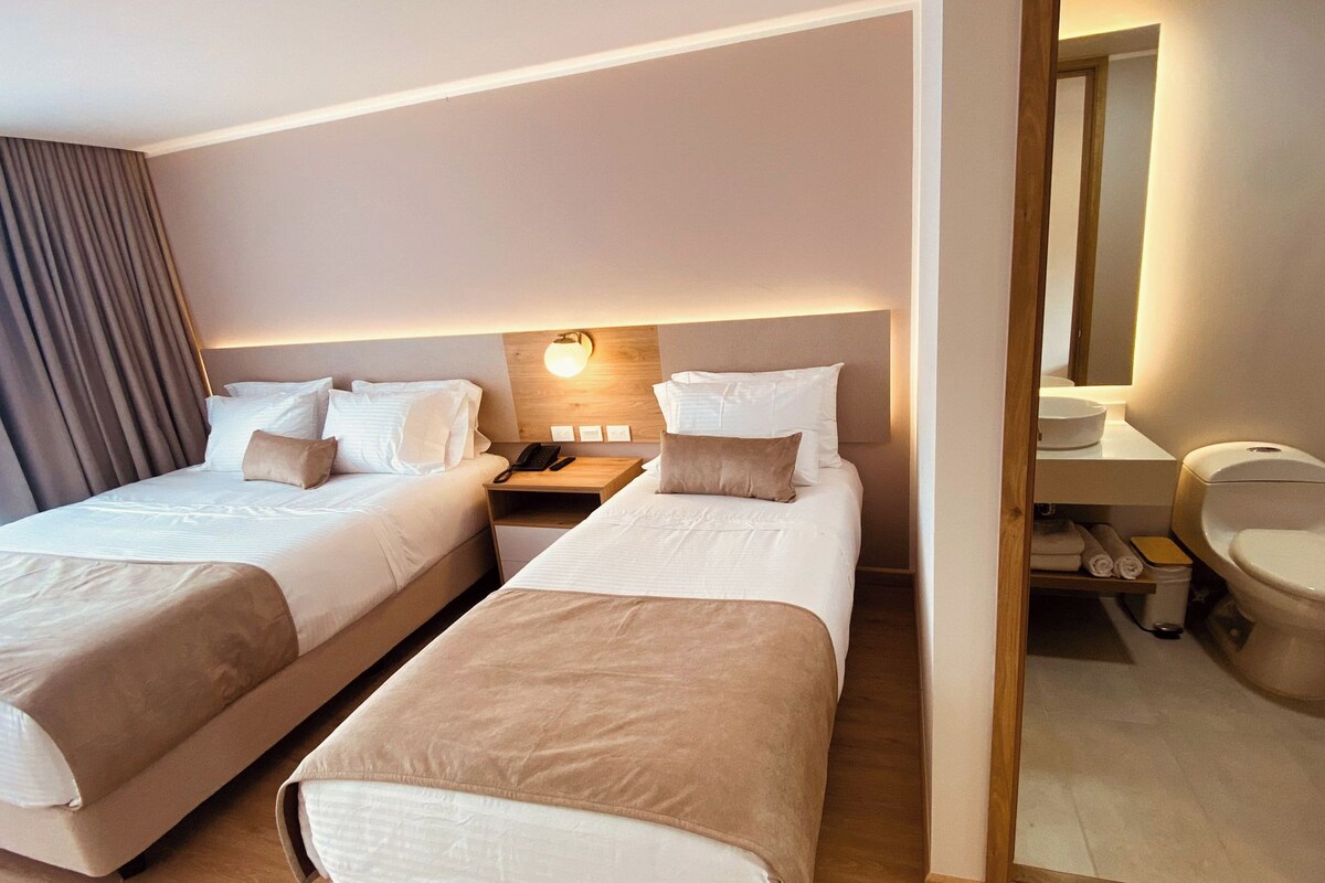 A hotel room with two beds, a bedside table with a lamp, a bathroom with a toilet and sink.