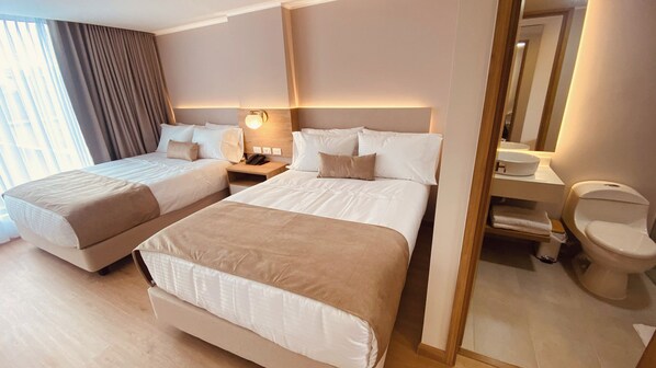 A hotel room with two beds, a bedside table with a lamp, a mirror, and a toilet.