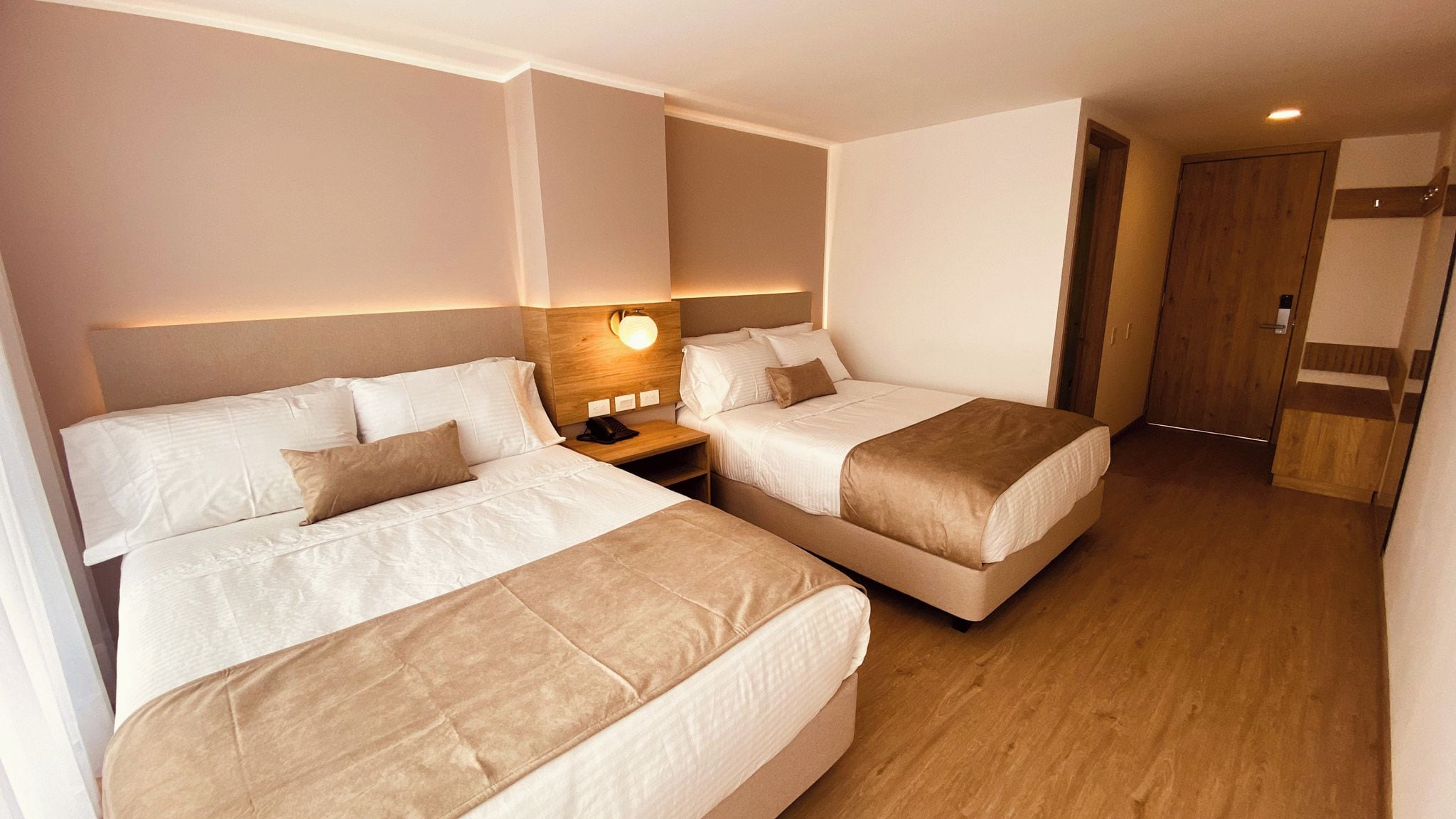 Habitación de hotel con dos camas, una mesita de noche, una lámpara de pared y un armario de madera.