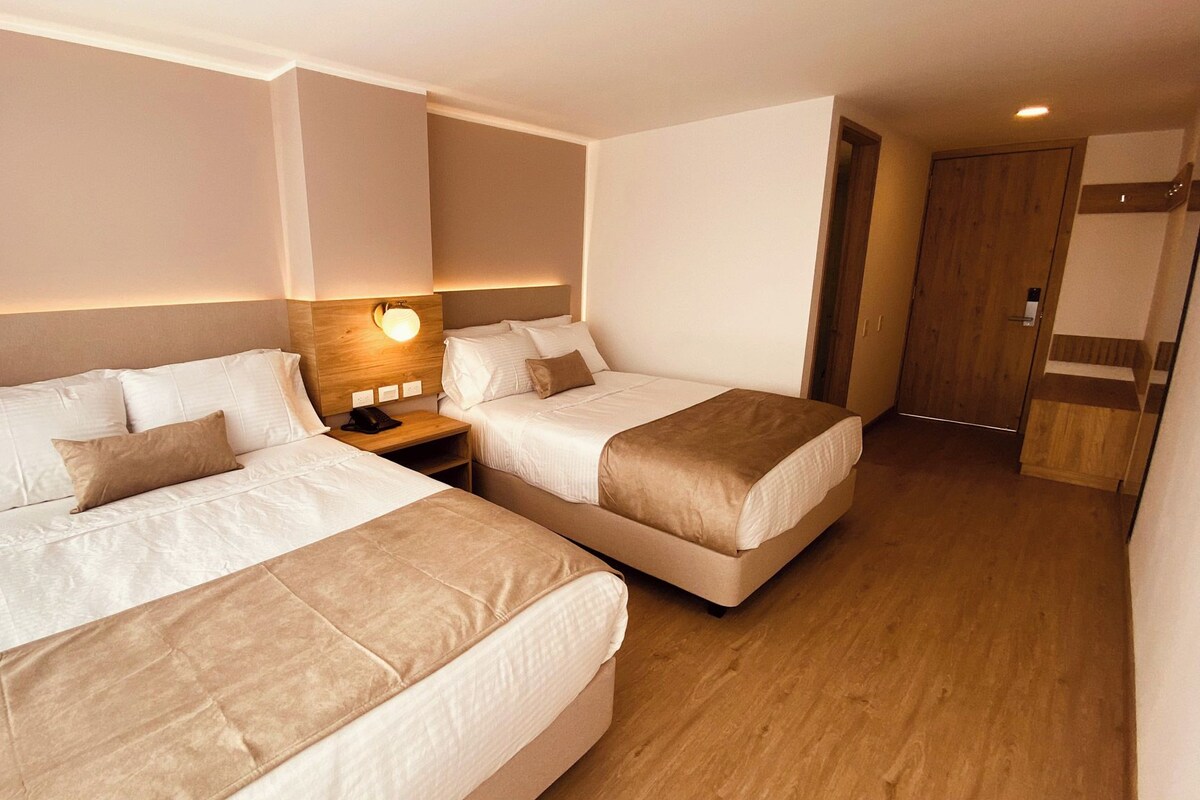 A hotel room with two beds, a nightstand, a wall-mounted lamp, and a wooden wardrobe.