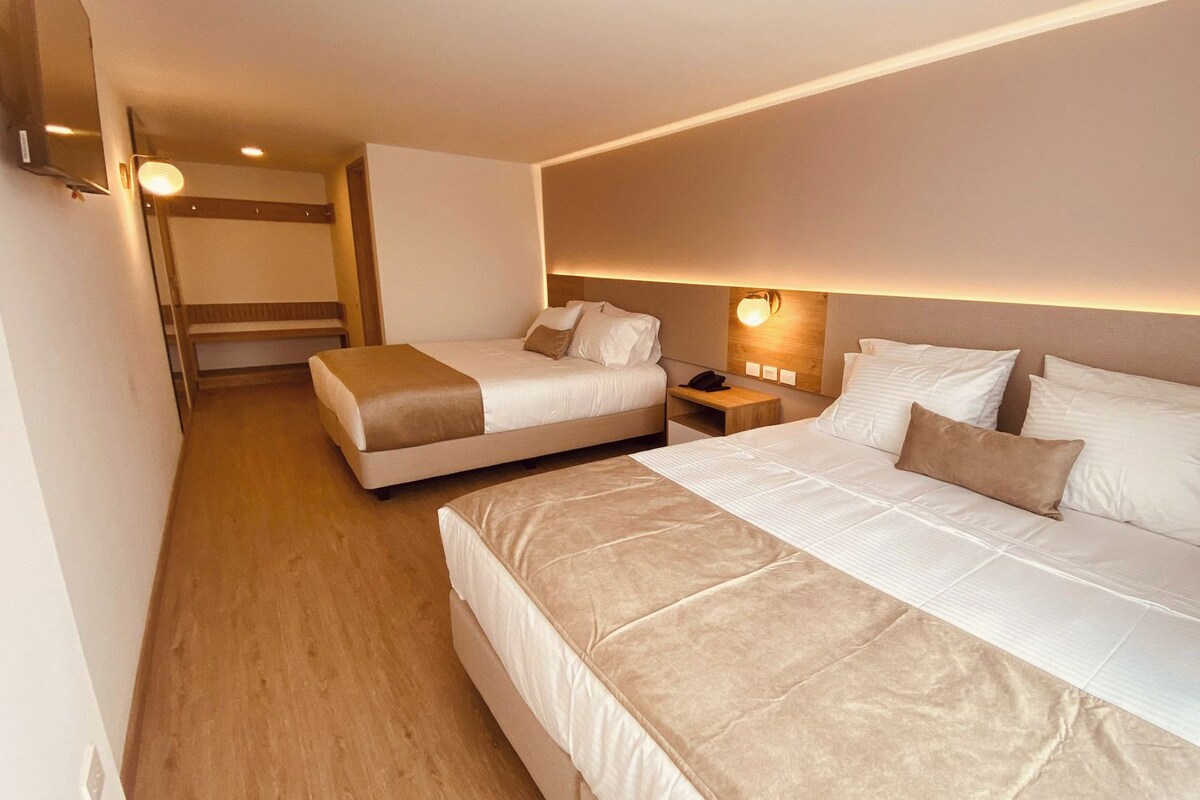 A hotel room with two beds, a bedside table, a lamp, and a wall-mounted light fixture.
