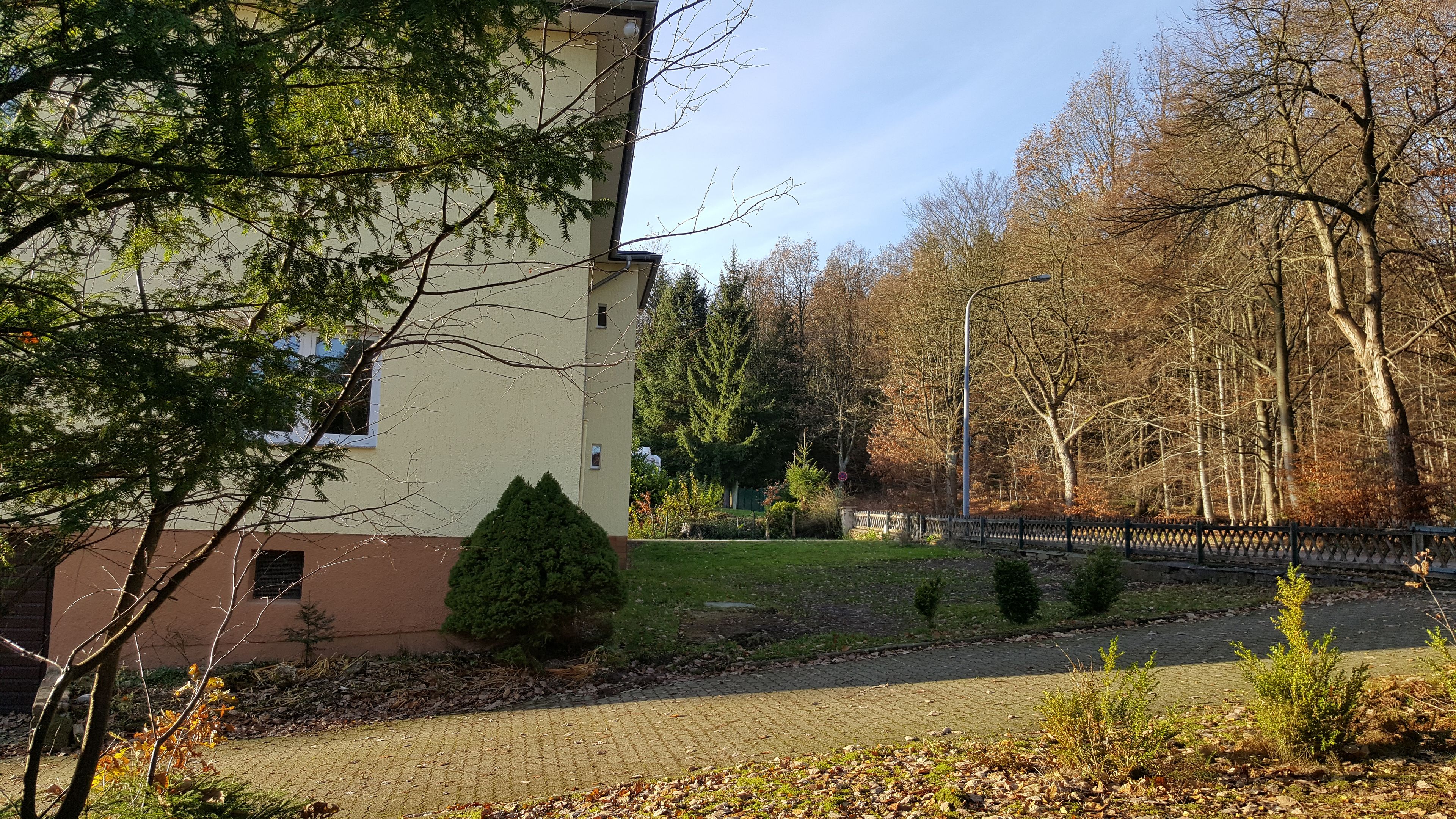 Ein Gebäude mit gepflasterter Auffahrt, kleinem Rasen und Zäunung.