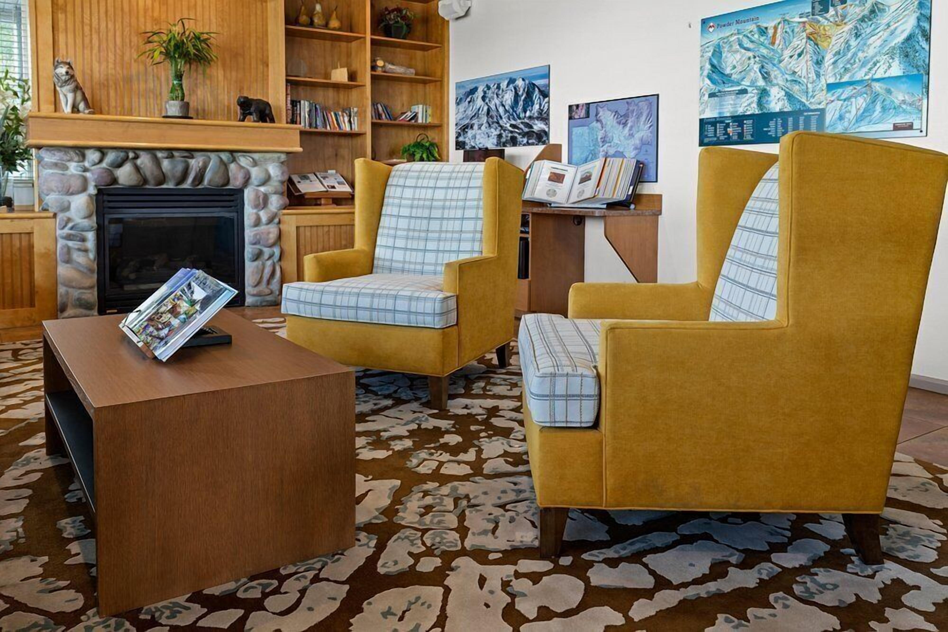 A living room with a fireplace, two yellow armchairs, a coffee table, and a bookshelf.