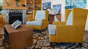 A living room with a fireplace, two yellow armchairs, a coffee table, and a bookshelf.