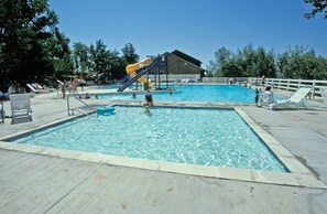 Piscina com escorregador, cadeiras de descanso e área coberta.