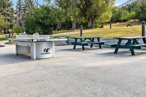 Un espace pique-nique avec des bancs verts et une table blanche portant la marque « Cornilleau ».