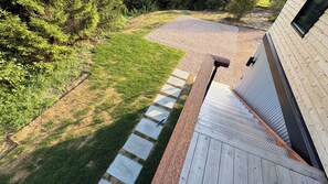A wooden deck with a stone pathway leading to a grassy area, surrounded by trees. - The Loft at Acadia Gateway (Trenton)