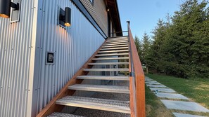 A metal staircase with a wooden handrail leading to a building with a corrugated metal exterior. - The Loft at Acadia Gateway (Trenton)