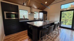 A modern kitchen with a central island, bar stools, a microwave, and a large window. - The Loft at Acadia Gateway (Trenton)