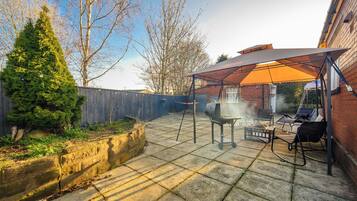 A backyard patio with a grill, outdoor furniture, and a covered seating area.