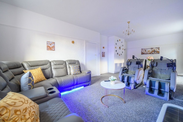 Una sala de estar moderna con un sofá gris, sillones de masaje, una mesita redonda y un reloj de pared.