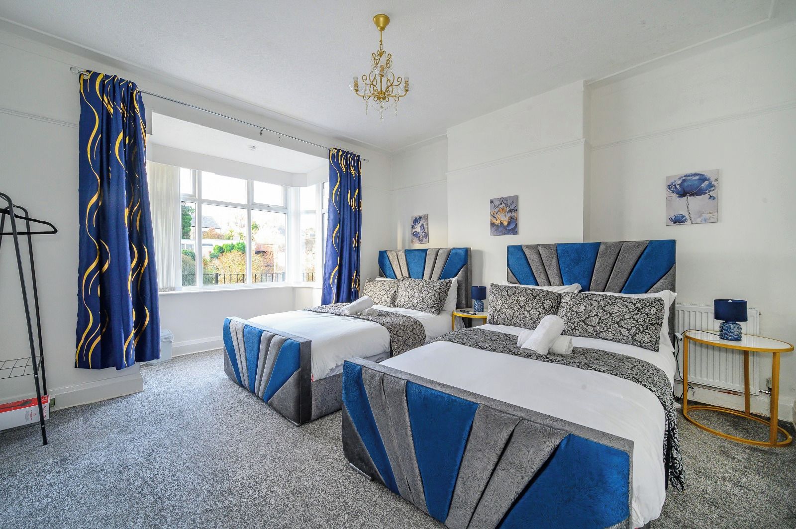 A hotel room with two beds, a chandelier, artwork on the walls, and a view through the window.