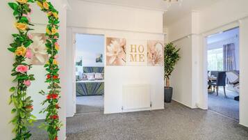 Een gang met een decoratieve bloemenstelling, een witte muur met een 'HOME' bord, en een uitzicht op een eetgedeelte.