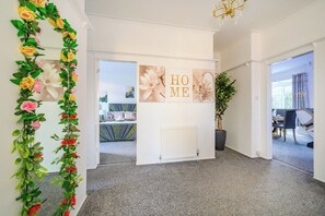 Un pasillo con un arreglo floral decorativo, una pared blanca con un letrero que dice 'HOME' y vistas hacia un comedor.