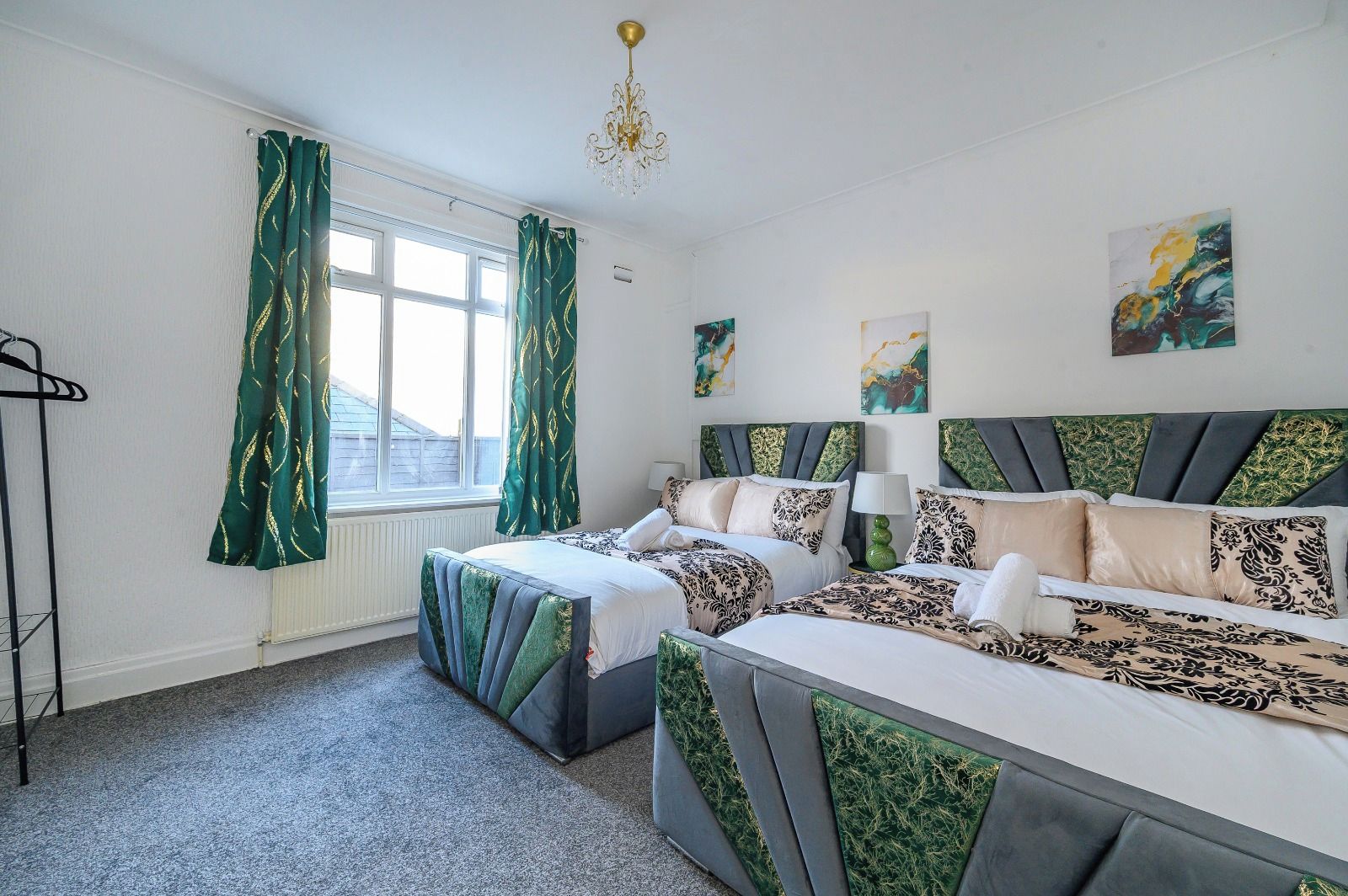 A hotel room with two beds, a radiator, a window with curtains, and artwork on the walls.