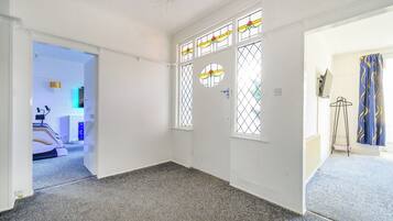 A room with a carpeted floor, a door with a window, and a hallway leading to another room.