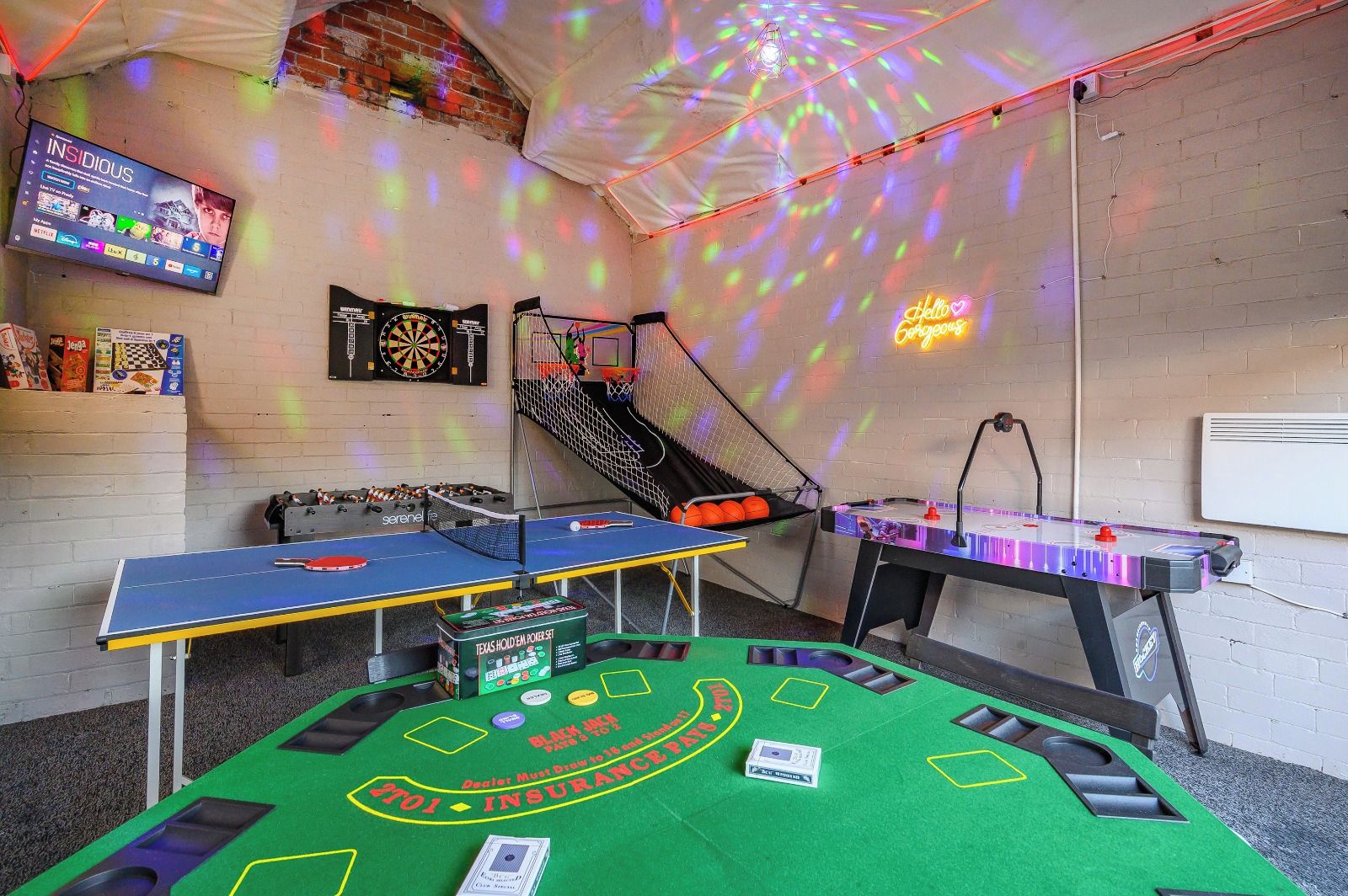 Una habitación con mesa de ping pong, mesa de futbolín, dardo y un letrero de neón.