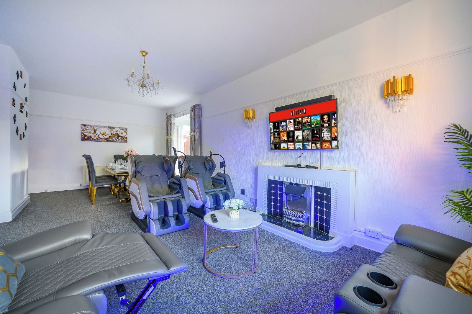 A living room with massage chairs, a fireplace, a Netflix screen, and a dining area.
