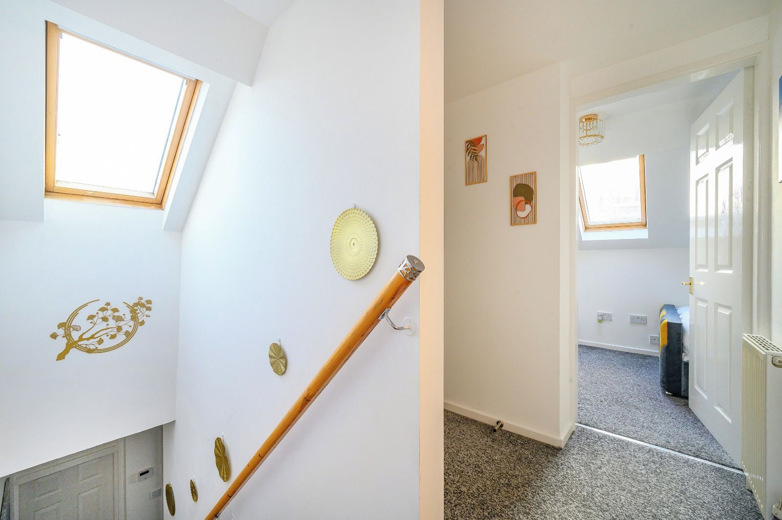 A room with a sloped ceiling, a wooden staircase, and a door leading to another room.
