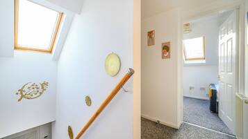 A room with a sloped ceiling, a wooden staircase, and a door leading to another room.