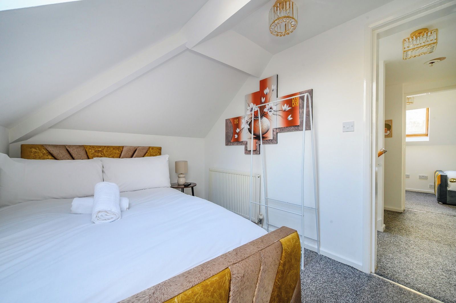 A hotel room with a bed, a radiator, a lamp, and artwork on the wall.